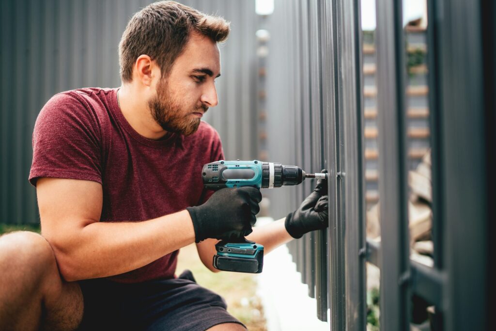 Caucasian construction man working with cordless electrical screwdriver on metal fence