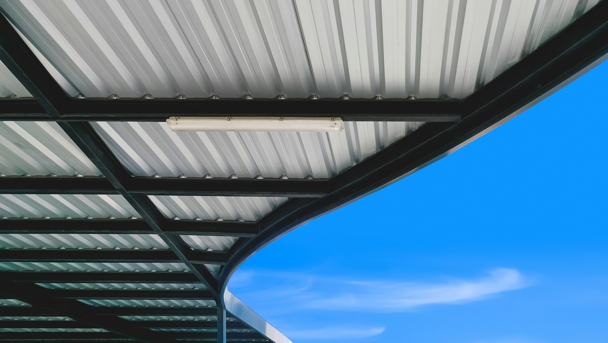 Modern corrugated metal curve roof of covered walkway and steel roof beam structure with blue sky