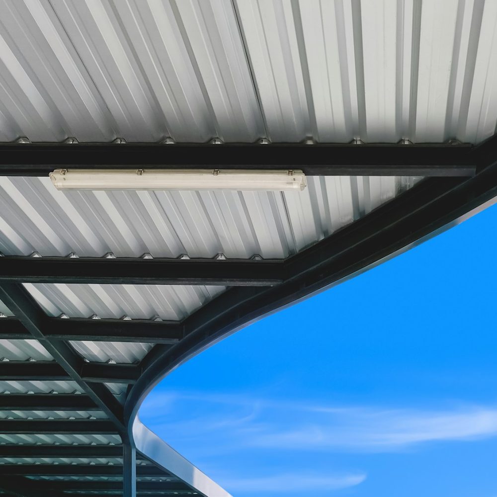 Modern corrugated metal curve roof of covered walkway and steel roof beam structure with blue sky